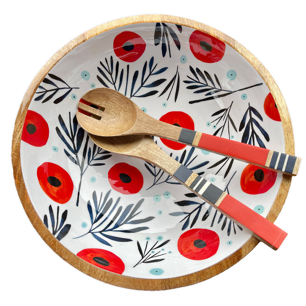Photo of a Mango Wood bowl with Red and Navy Watercolor Poppies on a field of white, with light blue berries interspersed throughout. Bowl has a large red stripe and a small white stripe handpainted on the exterior. To the side are a pair of coordinating, striped wooden tongs. Designed by Misha Zadeh for 180 Degrees