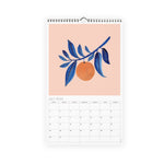 Misha Zadeh 2023 calendar. July spread featuring an orange hanging on a navy blue branch, against a peach background.