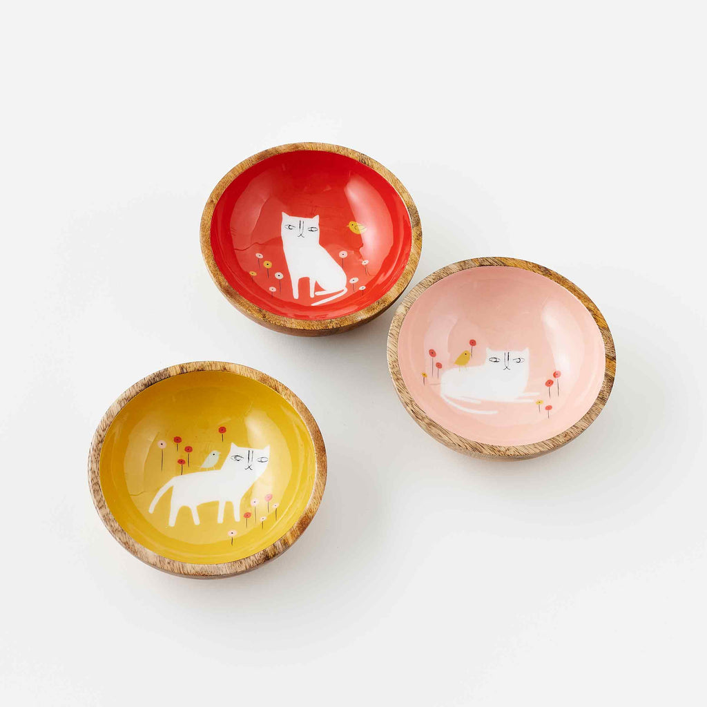 Three mango wood bowls with white cat artwork. One red, One pink, one yellow. With artwork by Misha Zadeh