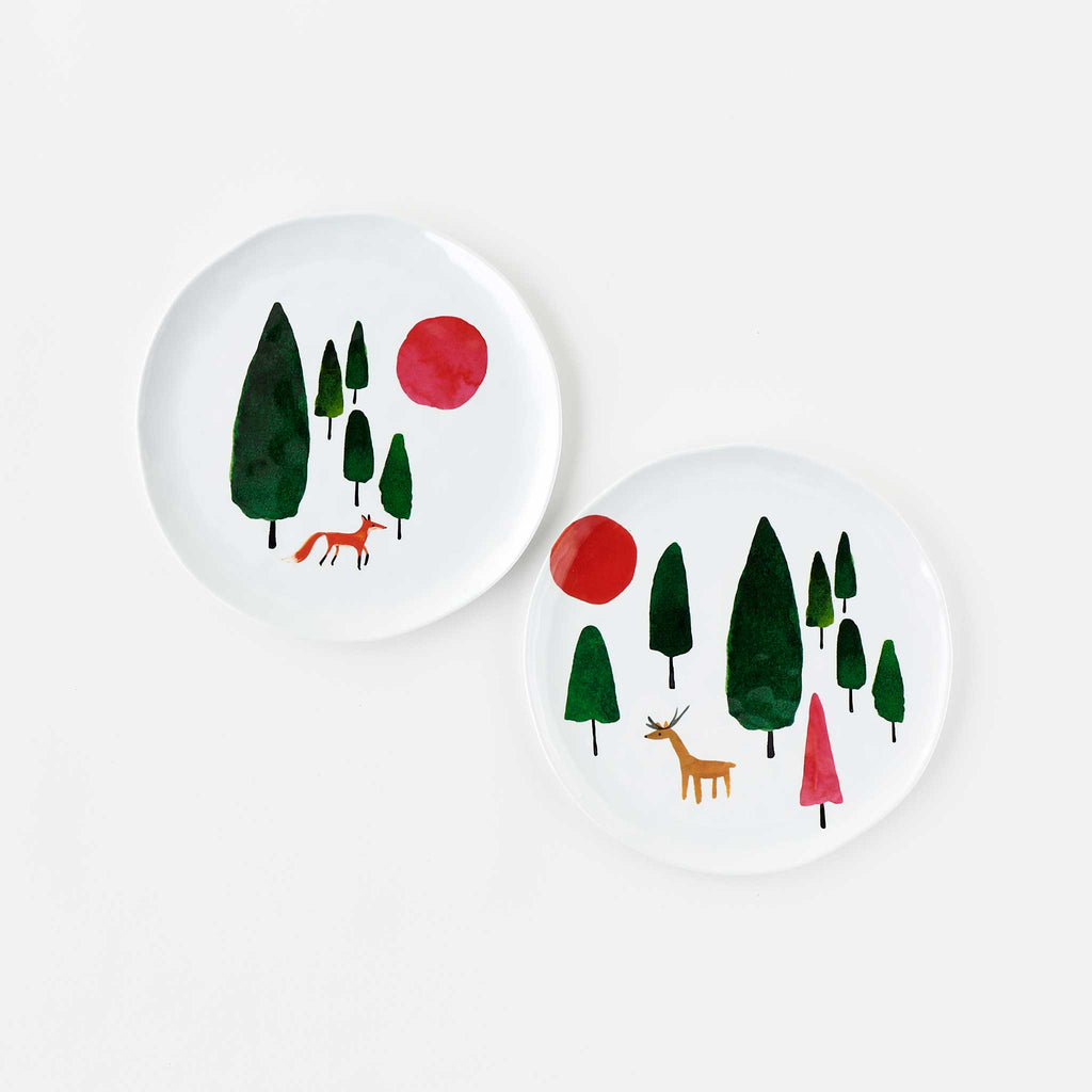 Misha Zadeh Winter Forest Melamine Plates featuring fox and deer with red and pink suns and rich green trees against a winter white wonderland
