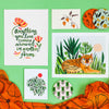 Misha Zadeh Lily Petals scarf in orange with art prints and coasters on a green background.