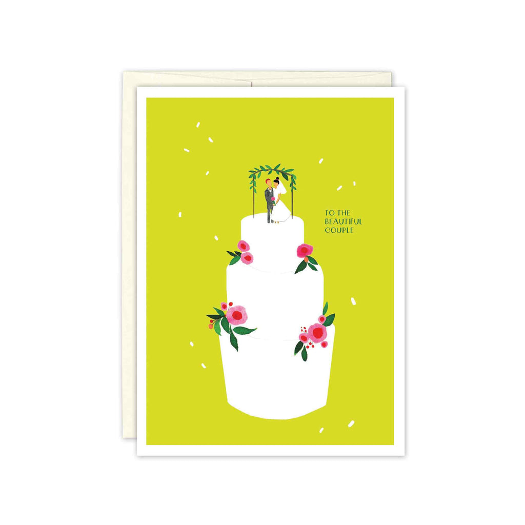 Three tiered white wedding cake with pink and red flowers on each tier. Top features a dark haired bride and a red haired groom figurine with a green leaf arch over them. White confetti or rice is flowing in the air and the background of the card is a bright lime green.