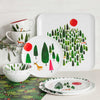 Misha Zadeh Winter Forest styled scene with a set of plates, bowls, and mugs and a large square platter up against a white background. Fern Forest wrapping paper sits on the table