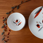 Misha Zadeh Winter Berries Holiday Ceramic table setting on a warm wood table top. Winterberry branch laying across the table